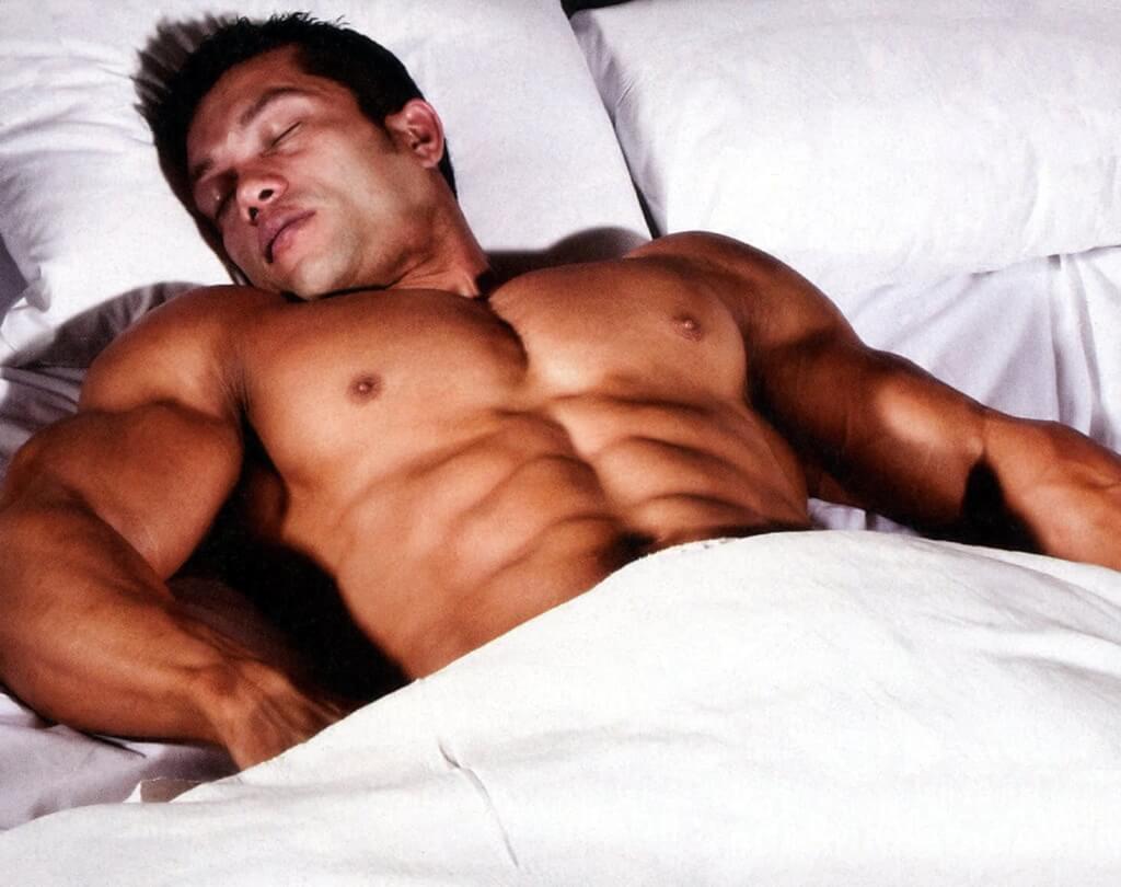 Накаченный мужчина спит в белой кровати