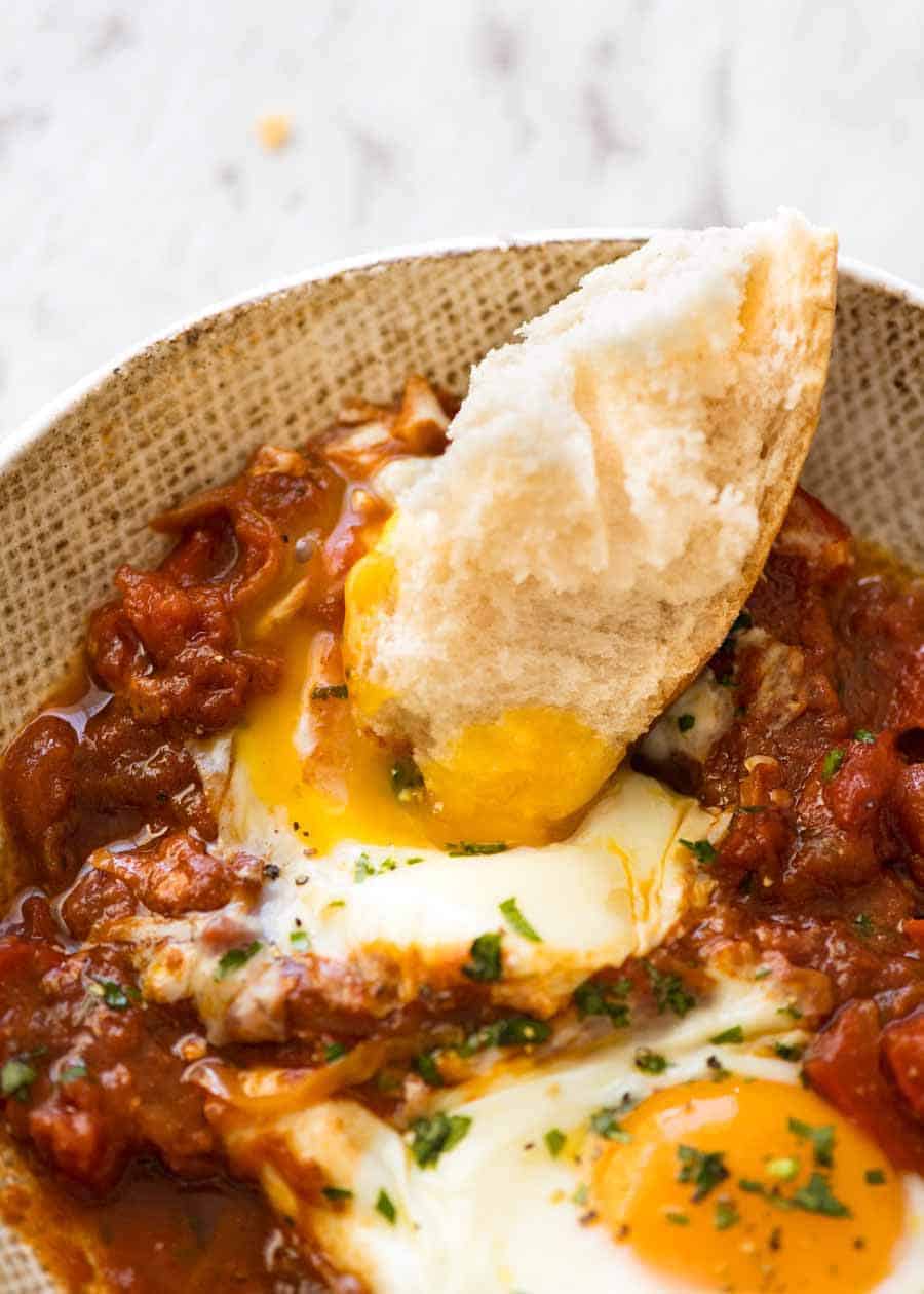 Bread being dunked into the runny yolks of Shakshuka, Middle Eastern baked eggs