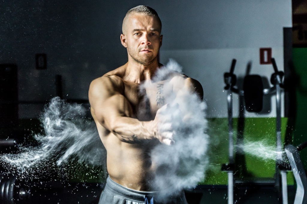 A man with his shirt off preparing to work out, clapping chalk powder into the air. If you