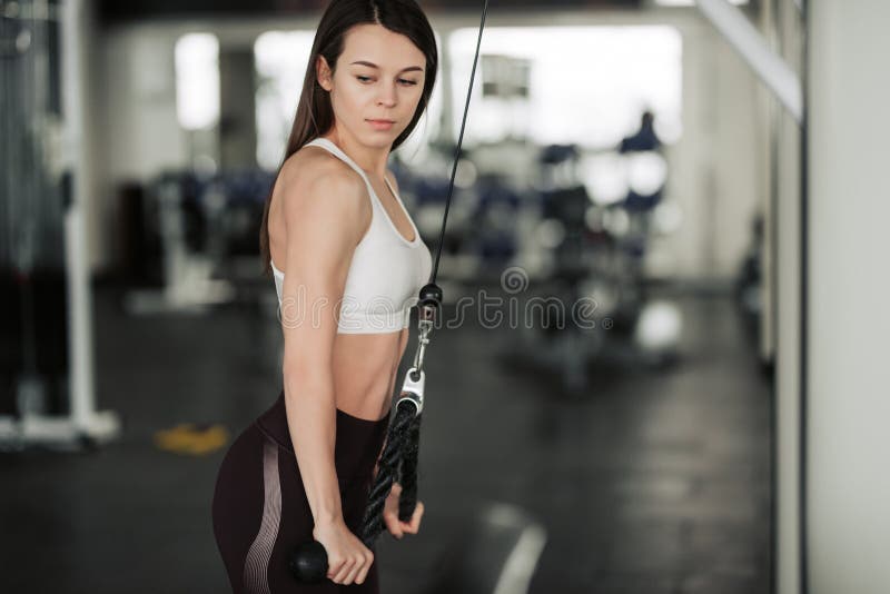 Athlete girl in sportswear working out and training her arms and shoulders with exercise machine in gym.  stock photography