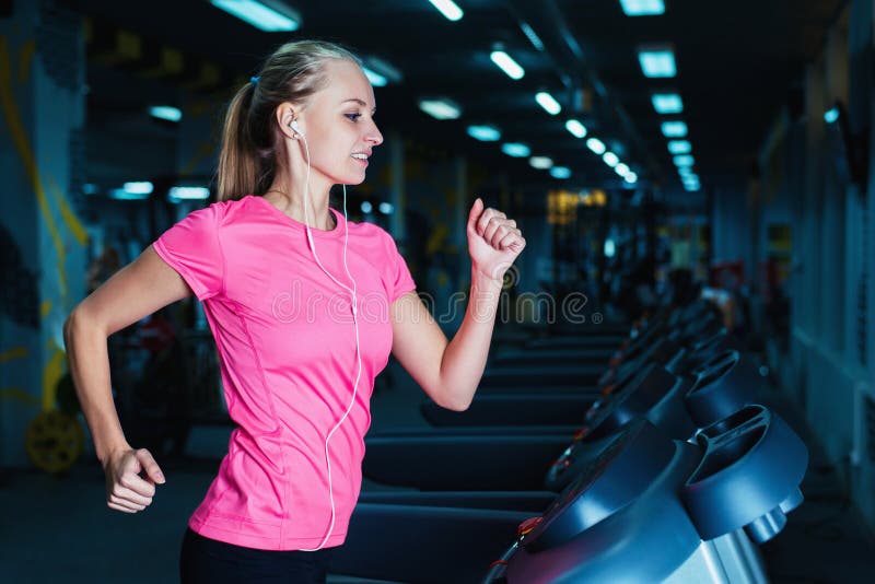 Attractive fitness girl running on machine treadmill. Pretty girl doing workout at modern fitness gym. stock photos