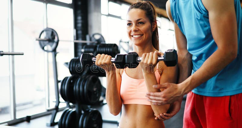 Beautiful woman doing exercises in gym with personal trainer. Beautiful women doing exercises for shoulders in gym with personal trainer stock image