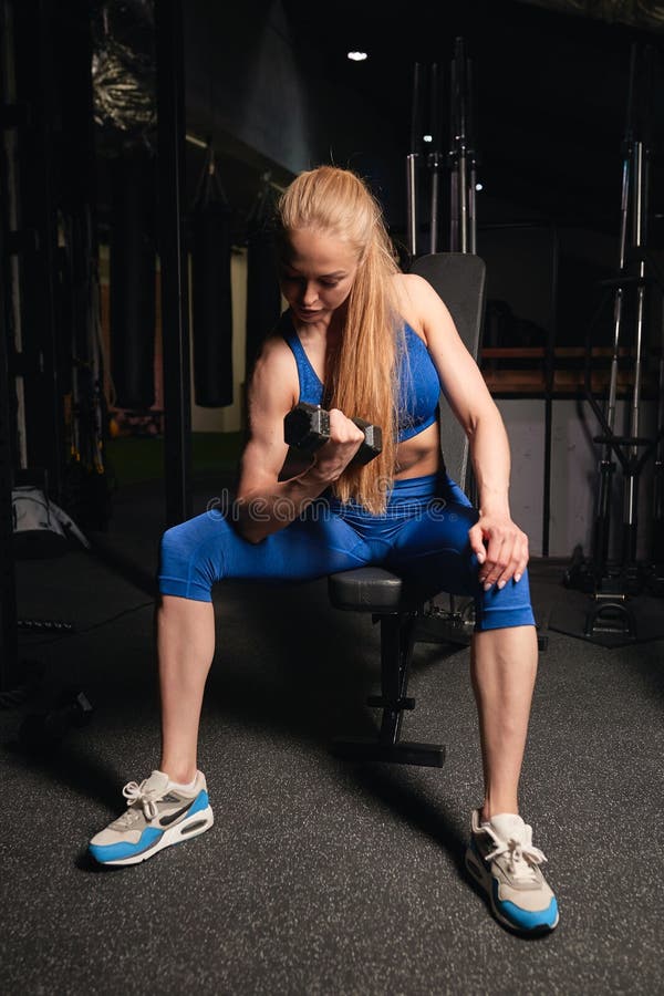 Blonde slim girl doing exercise with dumbbell on biceps and sitting on chair. Full length photo. willpower, motivation stock photos