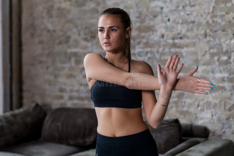 Fit young woman in sportswear doing shoulder and arm stretching exercise before workout indoors in loft apartment.  royalty free stock photos