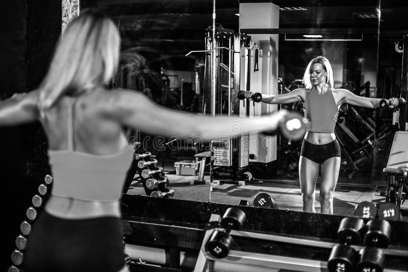 Fitness blonde girl posing and exercising with dumbbell. In gym stock image
