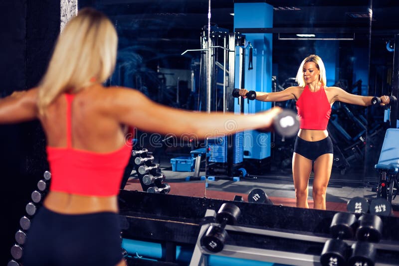 Fitness blonde girl posing and exercising with dumbbell. In gym royalty free stock photography