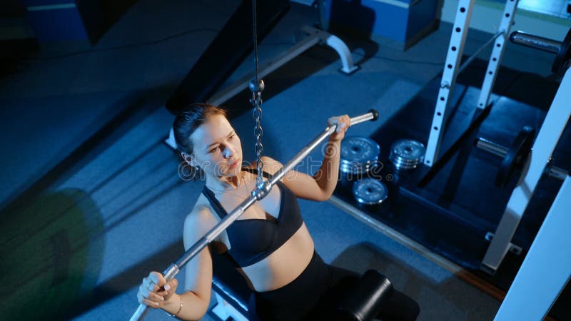 The girl is engaged in the gym. Traction upper unit on the simulator. stock photos