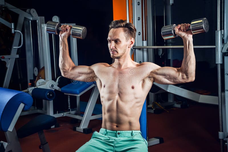 Handsome caucasian man working out at gym and doing shoulders exercises with dumbells. Handsome caucasian man working out at gym and doing shoulders exercises royalty free stock photo