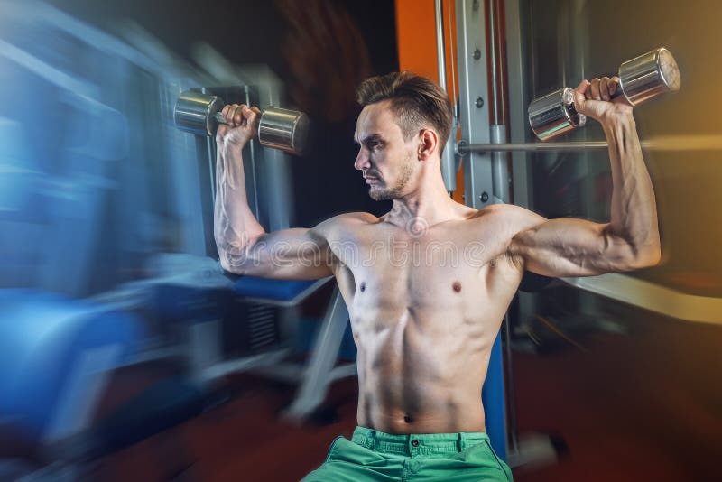 Handsome caucasian man working out at gym and doing shoulders exercises with dumbells. Handsome caucasian man working out at gym and doing shoulders exercises stock images