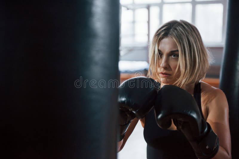 Holds arms, ready for the kick. Female boxer is punching the bag. Blonde have exercise in the gym.  royalty free stock photography