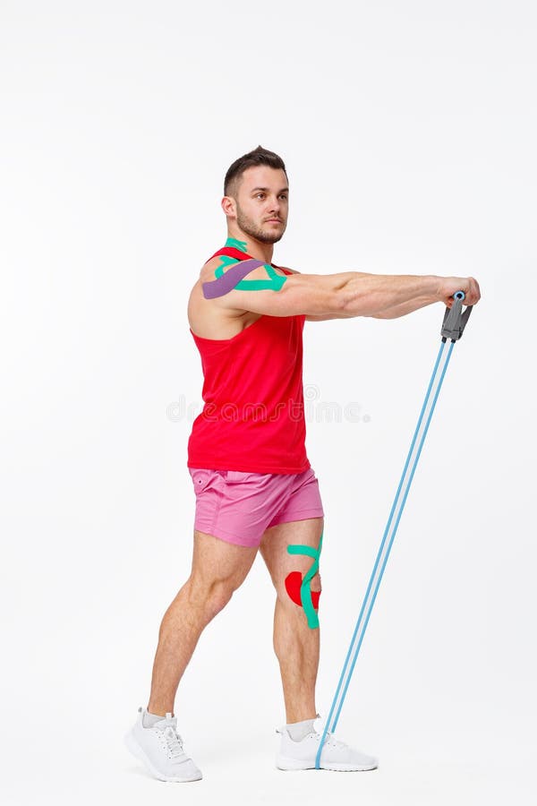 Kinesiology taping. Kinesiology tape on patient knee and shoulder. Young male athlete doing exercises with expender. Post traumatic rehabilitation, sport stock photo