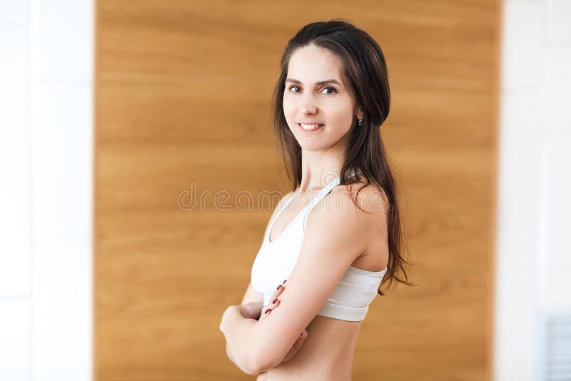 Portrait of positivity and pretty girl smiling at camera and posing with crossed arms in the gym. Seductive girl wearing in white. Sports wear, top and leggins stock image