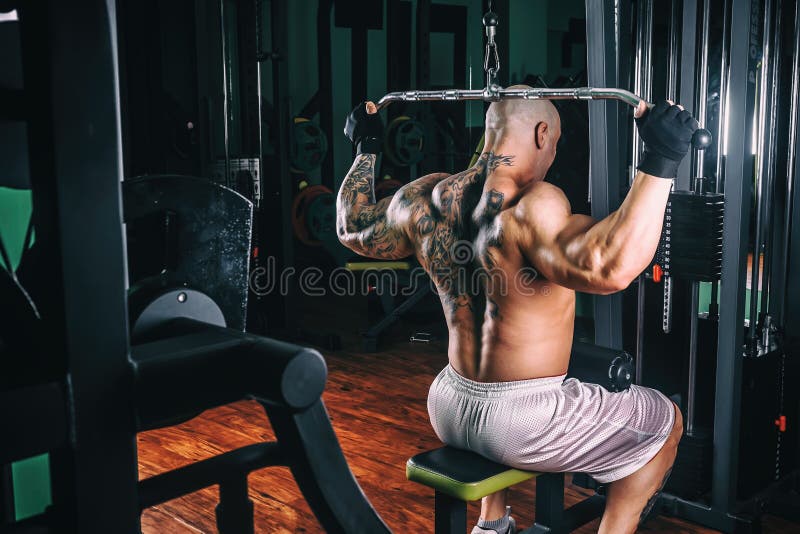 Power athletic guy bodybuilder, execute exercise with gym apparatus, on broadest muscle of back. Very power athletic guy bodybuilder, execute exercise with gym stock image