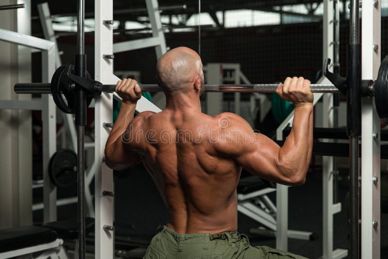 Shoulder Exercises On A Smith Machine. Mature Man Doing Shoulder Exercises In The Gym royalty free stock images