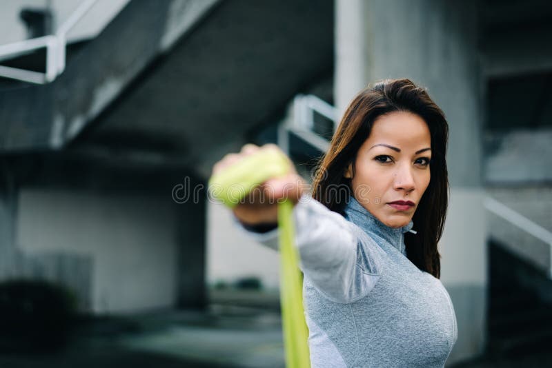 Strong woman doing shoulder raises exercise with resistance band. Motivated latin woman doing shoulder raises exercise with fitness resistance band. Urban stock images