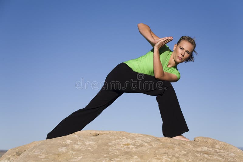 Yoga woman leaning forward. A woman doing yoga position prayer twist while standing on a rock with the blue sky royalty free stock images