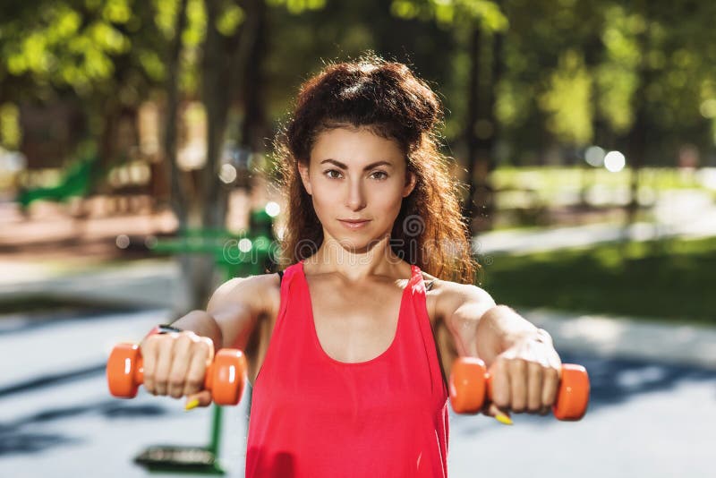 Young woman exercises shoulders with dumbbells outdoors on a warm sunny morning. Healthy lifestyle concept royalty free stock photos