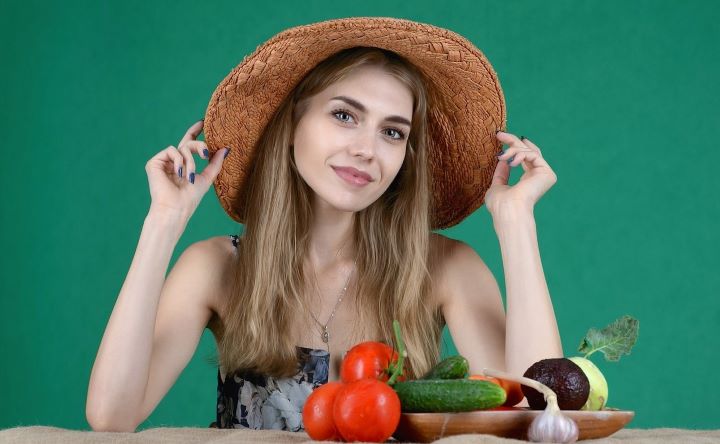 Девушка в шляпе сидит у стола с овощами
